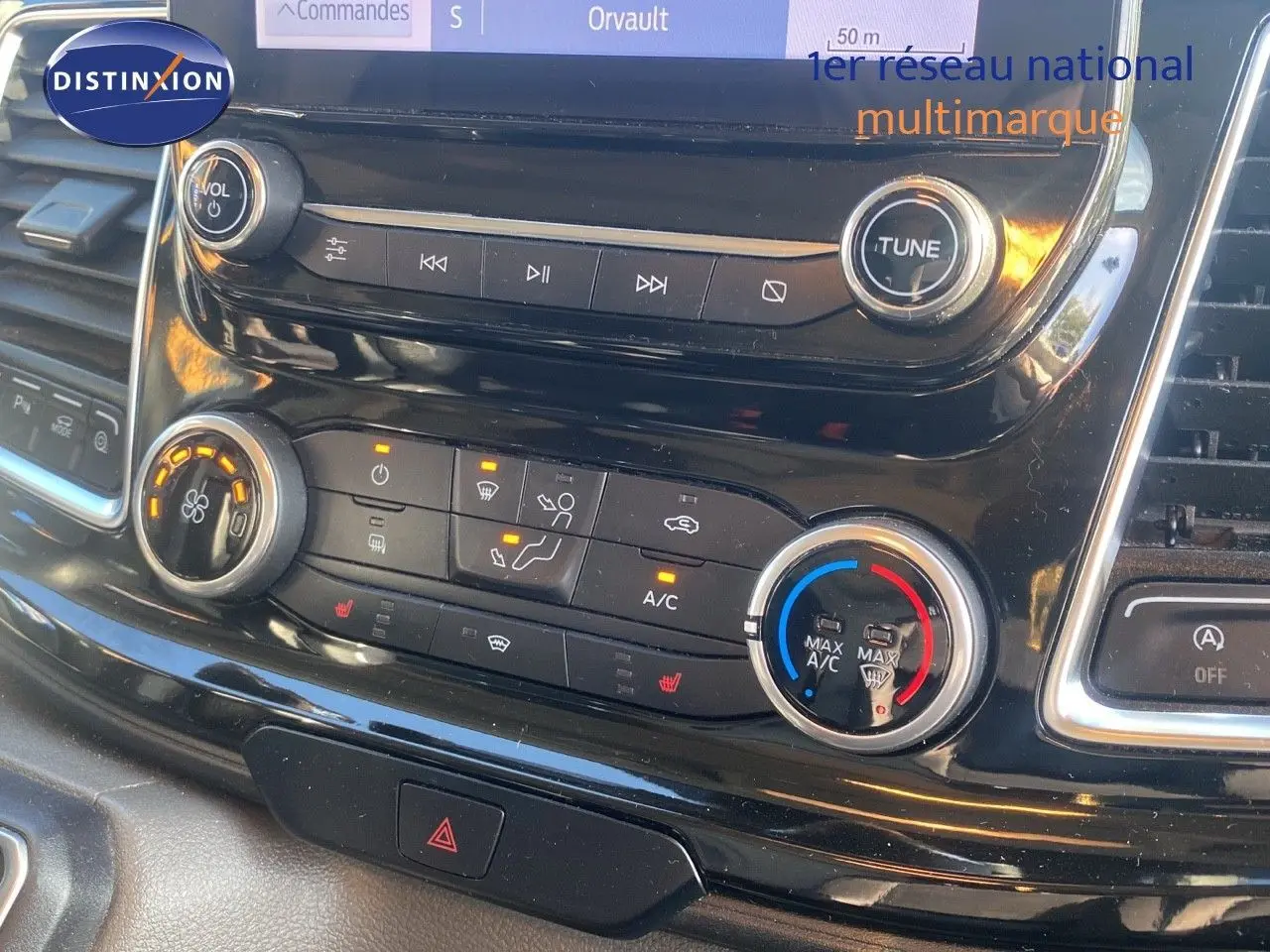 Gros plan sur la console centrale noire du Ford Transit Custom gris, montrant les commandes de climatisation et multimédia.
