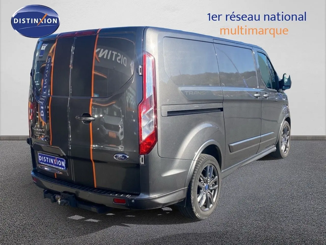 Vue 3/4 arrière droit du Ford Transit Custom gris magnetic avec jantes sport et bandes orange sur les portes arrière.
