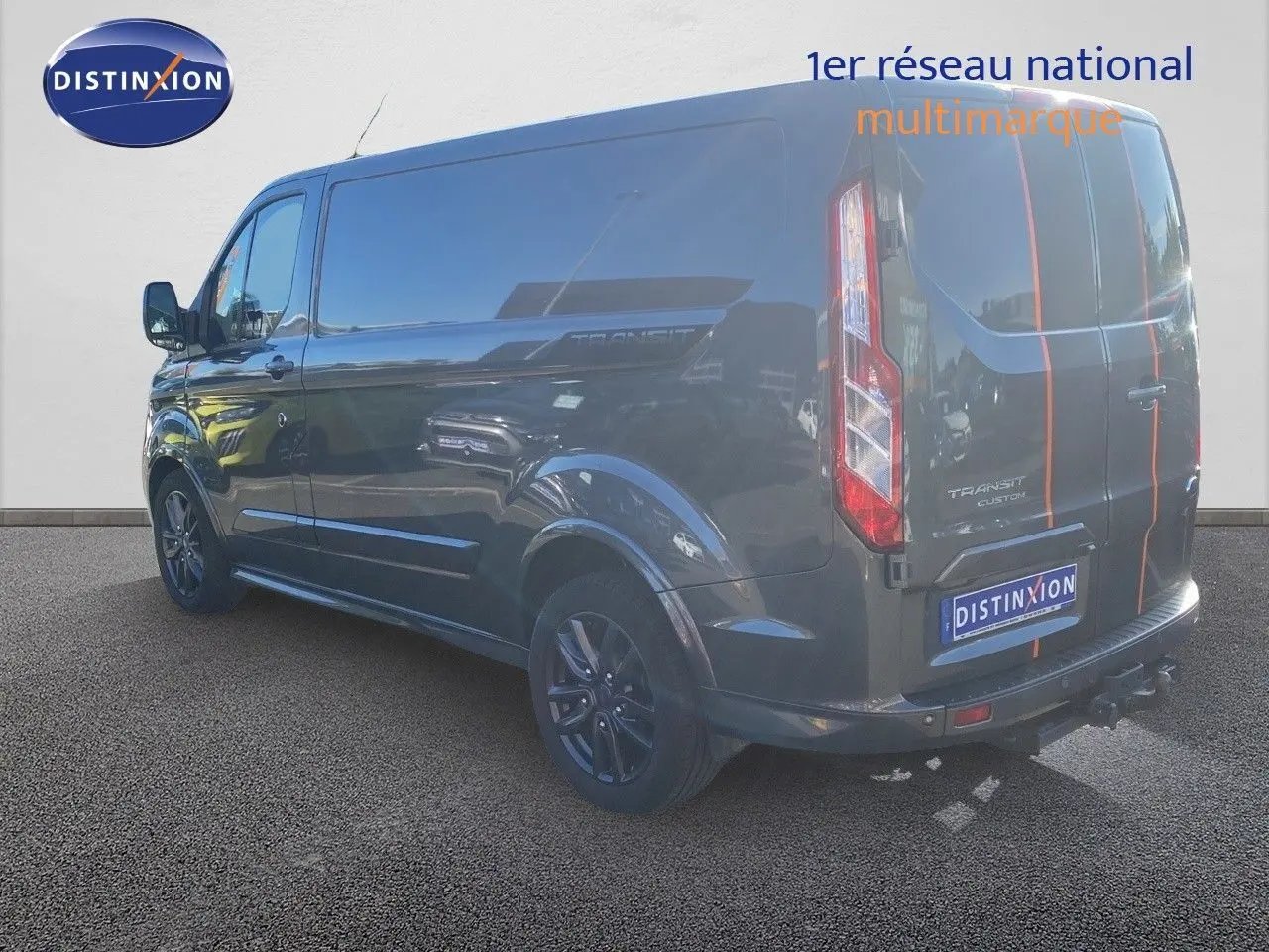 Vue 3/4 arrière droite du Ford Transit Custom gris magnetic avec bandes orange et jantes noires sport.