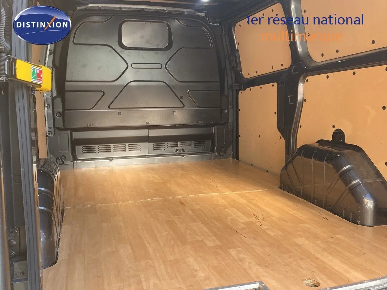 Vue intérieure du fourgon Ford Transit Custom L1H1 2023, montrant l'espace de chargement avec plancher bois clair et parois protégées.