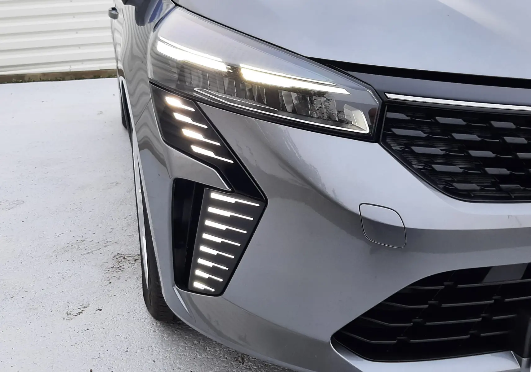 Gros plan sur l'avant gauche de la Renault Clio V gris schiste, mettant en valeur ses feux LED distinctifs allumés.