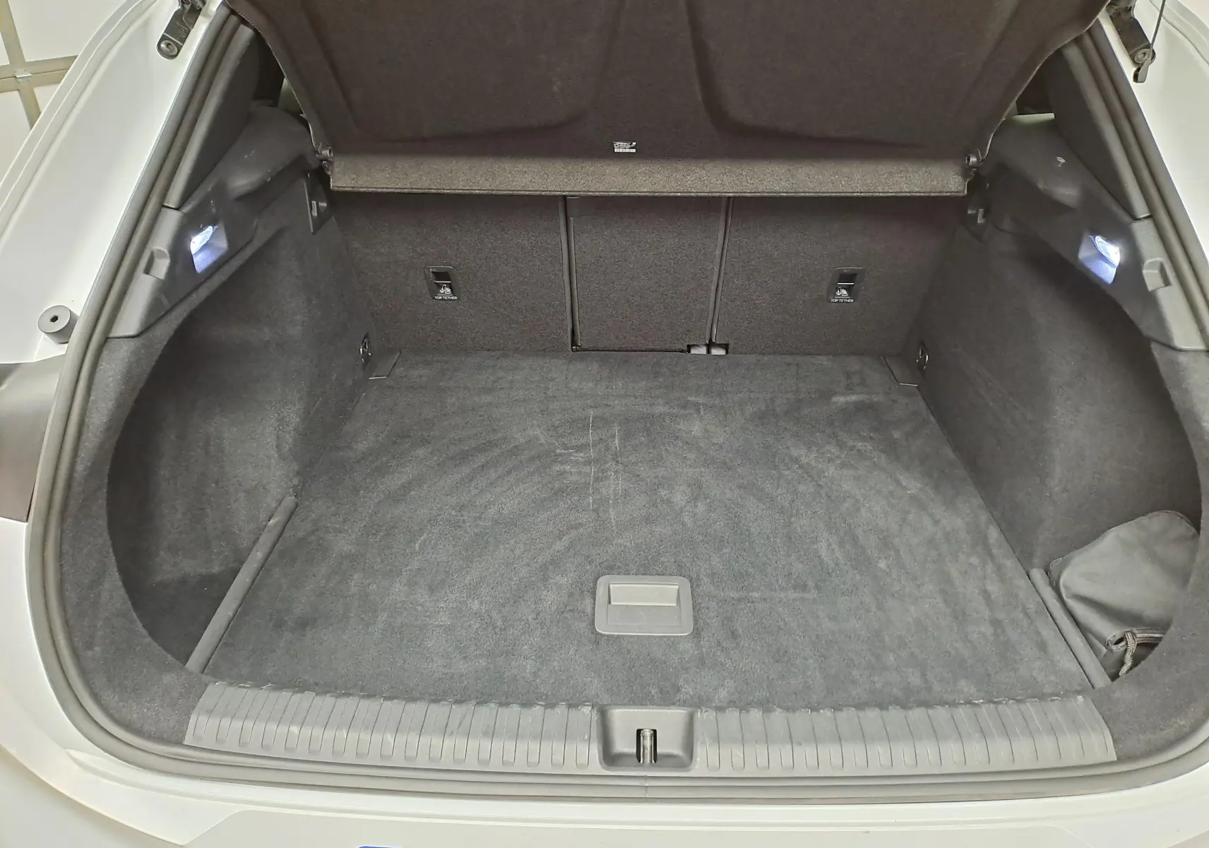 Coffre ouvert d'une CUPRA TERRAMAR blanc Nevada, vue de l'arrière montrant l'espace de chargement vide et l'éclairage intérieur.