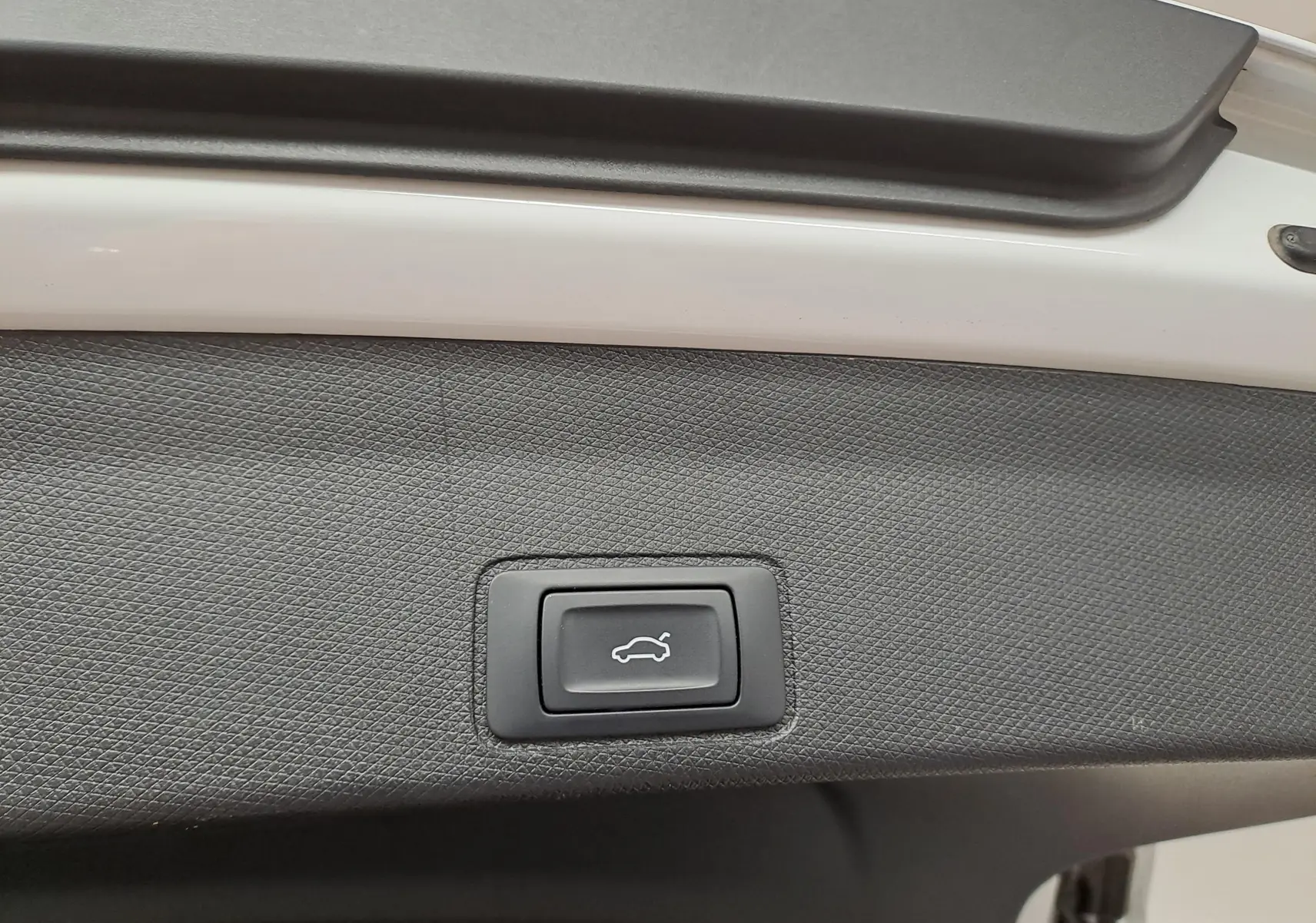 Gros plan sur le bouton d'ouverture électrique du coffre sur la porte arrière du CUPRA TERRAMAR blanc Nevada.