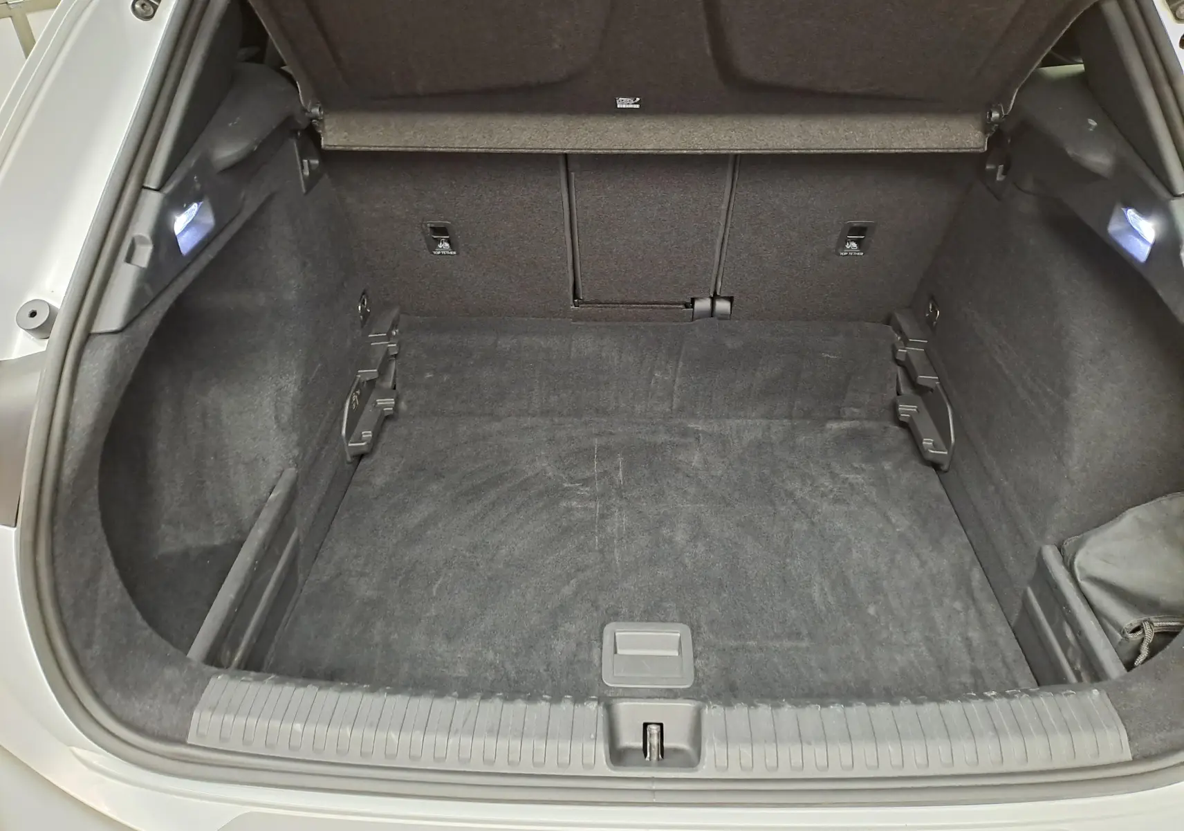 Coffre ouvert vu de l'arrière d'une CUPRA TERRAMAR blanc Nevada, intérieur noir avec éclairage latéral.