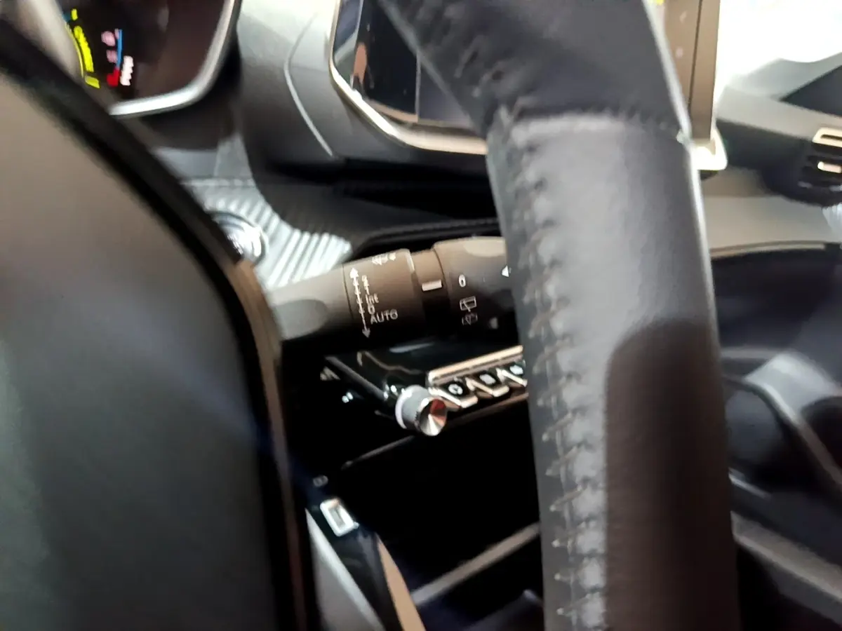 Gros plan intérieur sur le volant cuir et la commande des essuie-glaces de la Peugeot 208 électrique blanche.
