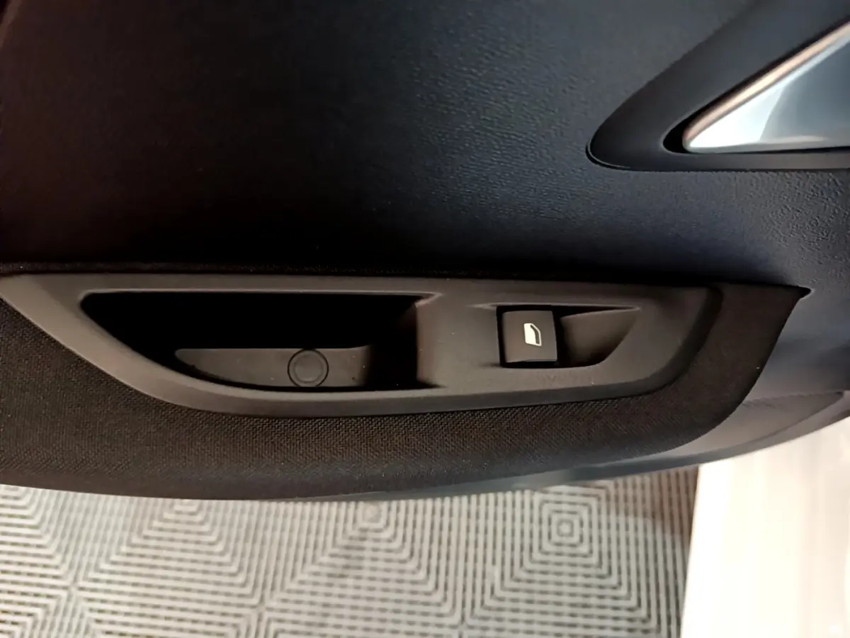 Détail intérieur du panneau de porte côté conducteur noir avec bouton de commande de vitre sur Peugeot 208 Electrique blanche.
