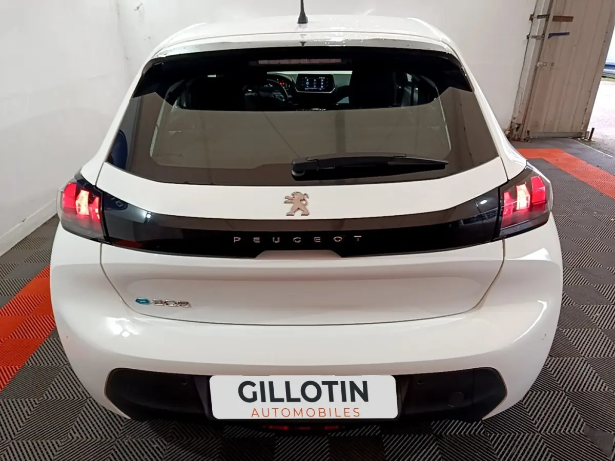 Vue arrière d'une Peugeot 208 électrique blanche avec feux LED allumés et bande noire distinctive sur le hayon.
