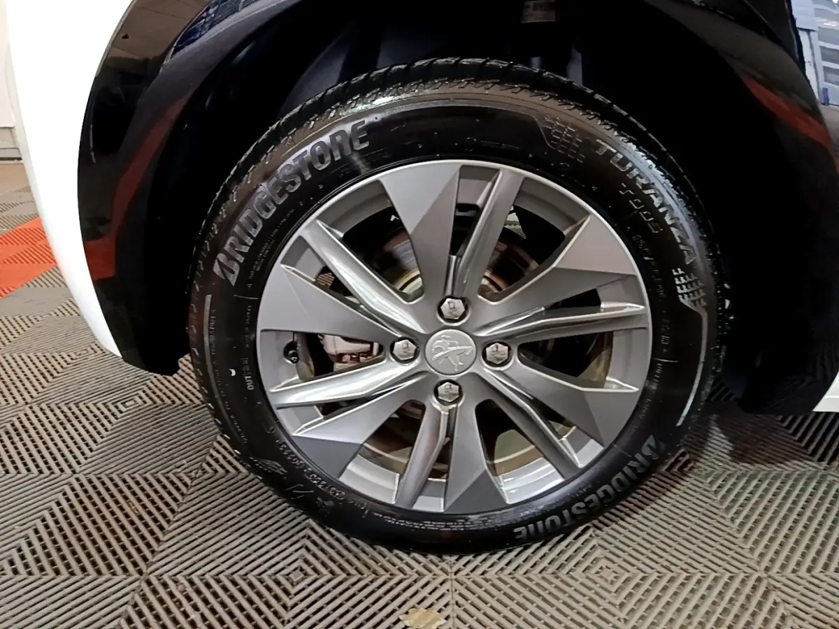 Gros plan sur la roue avant droite d’une Peugeot 208 électrique blanche avec jante alliage gris et pneu Bridgestone.