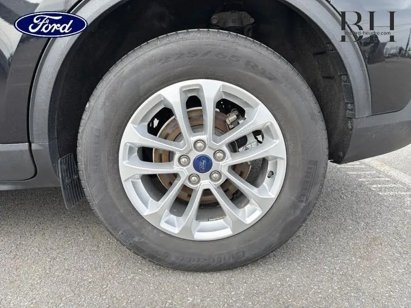 Gros plan sur la roue avant droite du Ford Kuga noir Agate Métallisée avec jante alliage et logo Ford central.