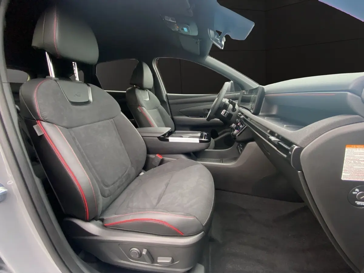 Intérieur avant du Hyundai Tucson gris foncé, sièges noirs avec surpiqûres rouges et tableau de bord moderne.