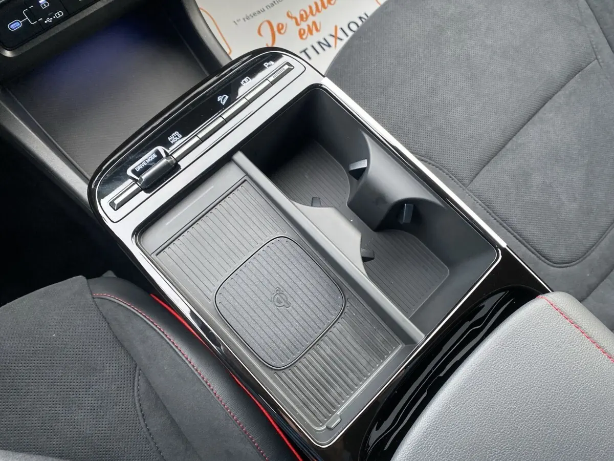 Vue rapprochée de la console centrale noire du Hyundai Tucson 1.6 Hybrid N Line avec porte-gobelets et chargeur sans fil.