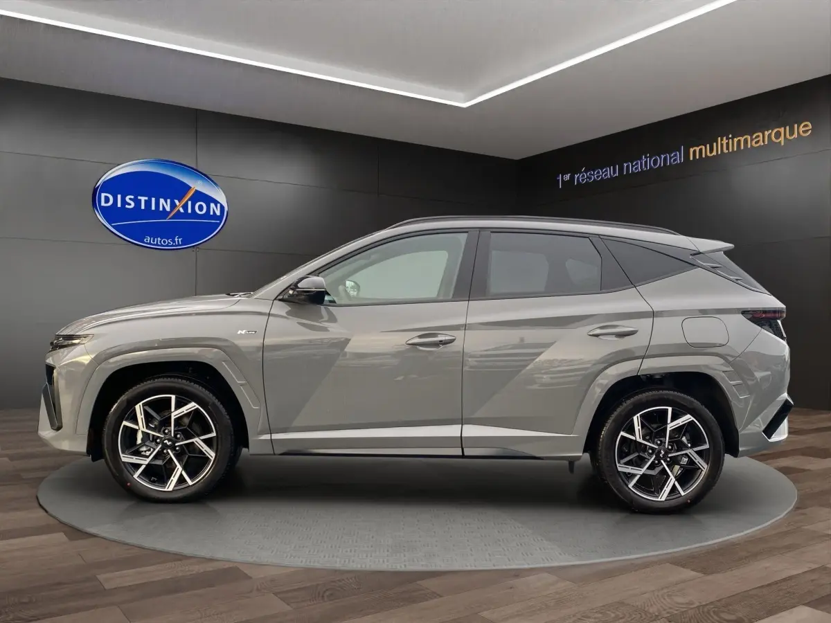 Profil côté gauche d'un Hyundai Tucson gris foncé 2026 N Line Creative en showroom avec jantes alliage noires et argentées.