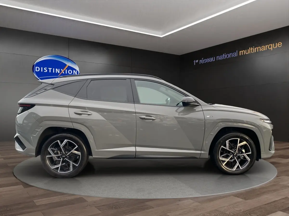 Vue de profil côté gauche d'un Hyundai Tucson gris foncé 2026, avec jantes alliage et lignes anguleuses marquées.