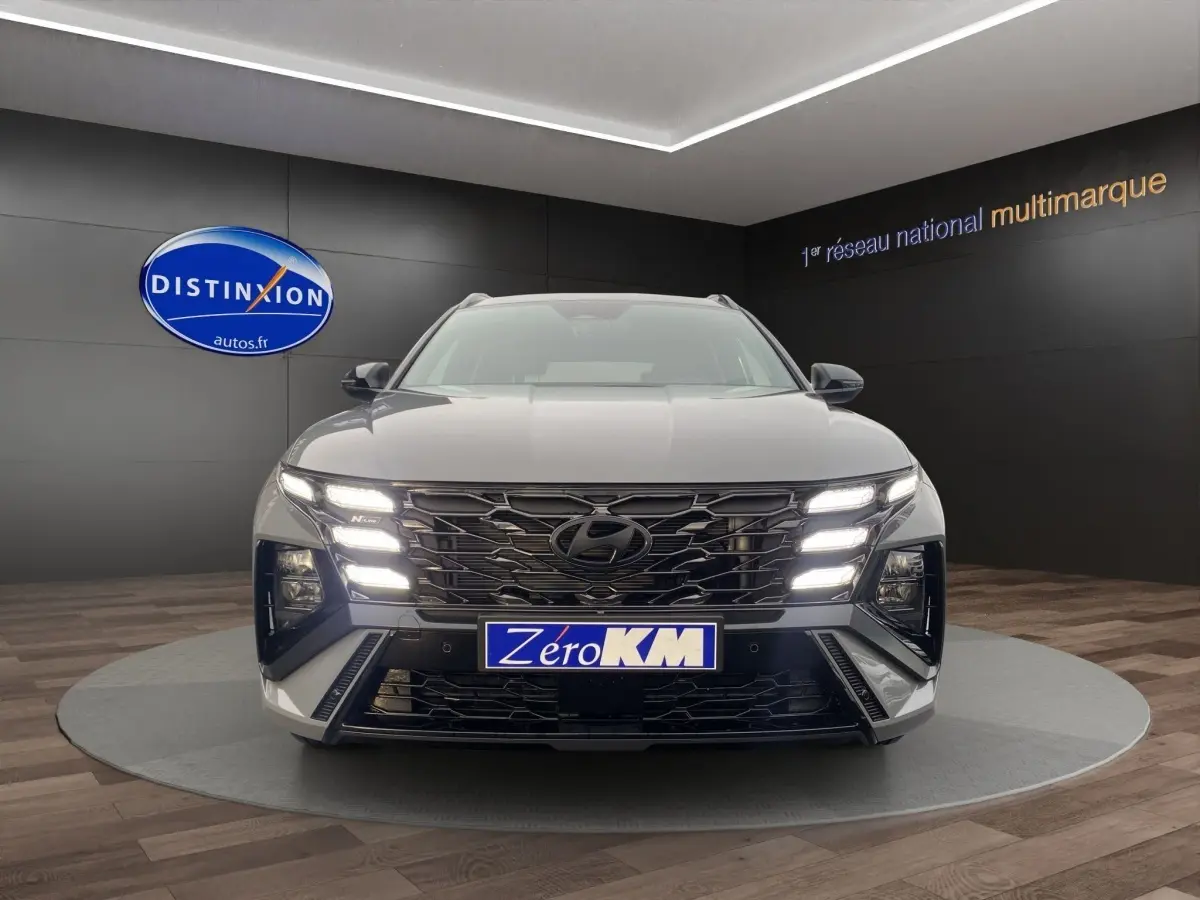 Vue avant d'un Hyundai Tucson gris foncé avec calandre noire et feux LED allumés en showroom.
