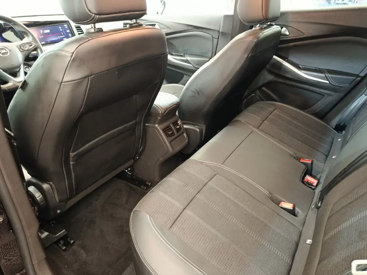 Vue intérieure arrière de l’Opel Grandland hybride 2023, sièges noirs en cuir et tissu avec console centrale et aérateurs.