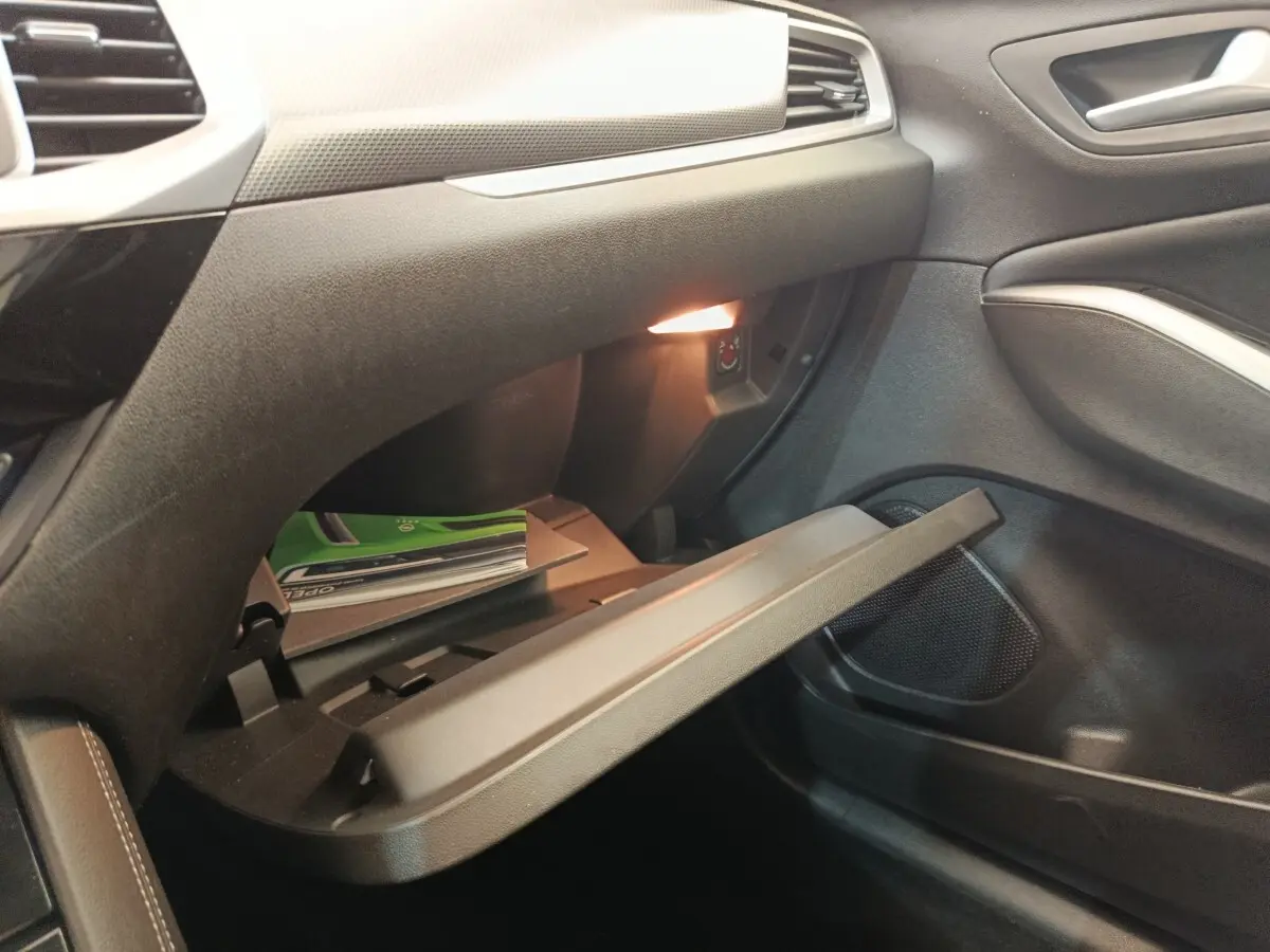 Gros plan de la boîte à gants ouverte côté passager de l’Opel Grandland hybride noire, avec éclairage intérieur allumé.