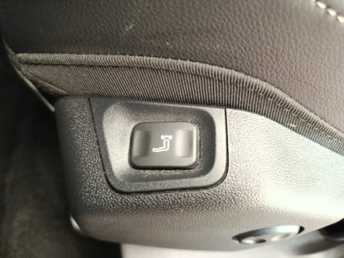 Bouton de réglage électrique de l'inclinaison du siège avant, sur revêtement noir texturé.
