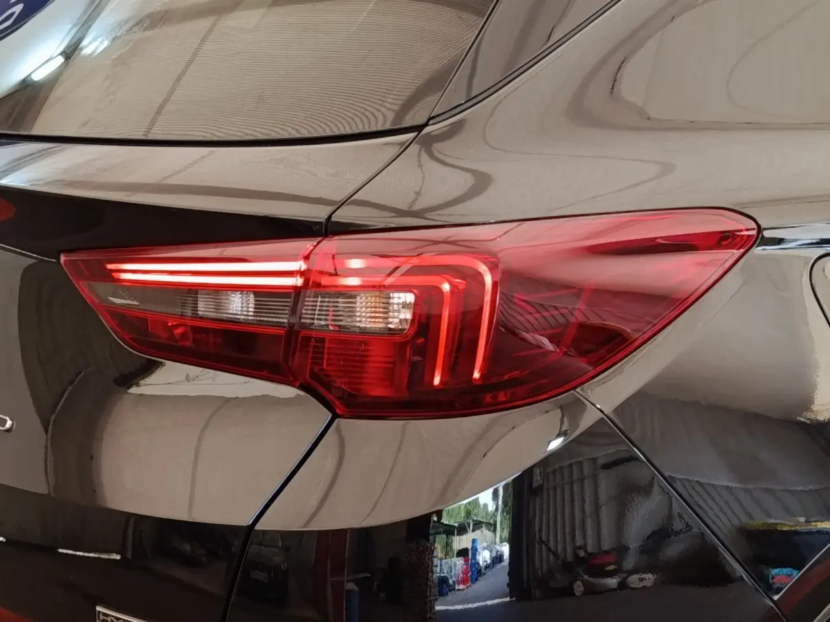 Gros plan sur le feu arrière droit rouge d’un Opel Grandland hybride rechargeable noir 2023, reflet d’atelier visible.