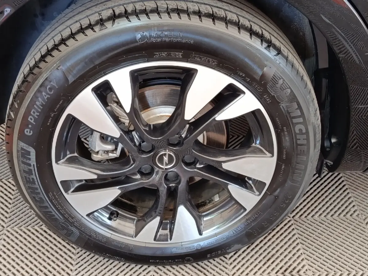 Gros plan sur la jante alliage bicolore noir et argent avec logo Opel, montée sur pneu Michelin d’un Opel Grandland noir.