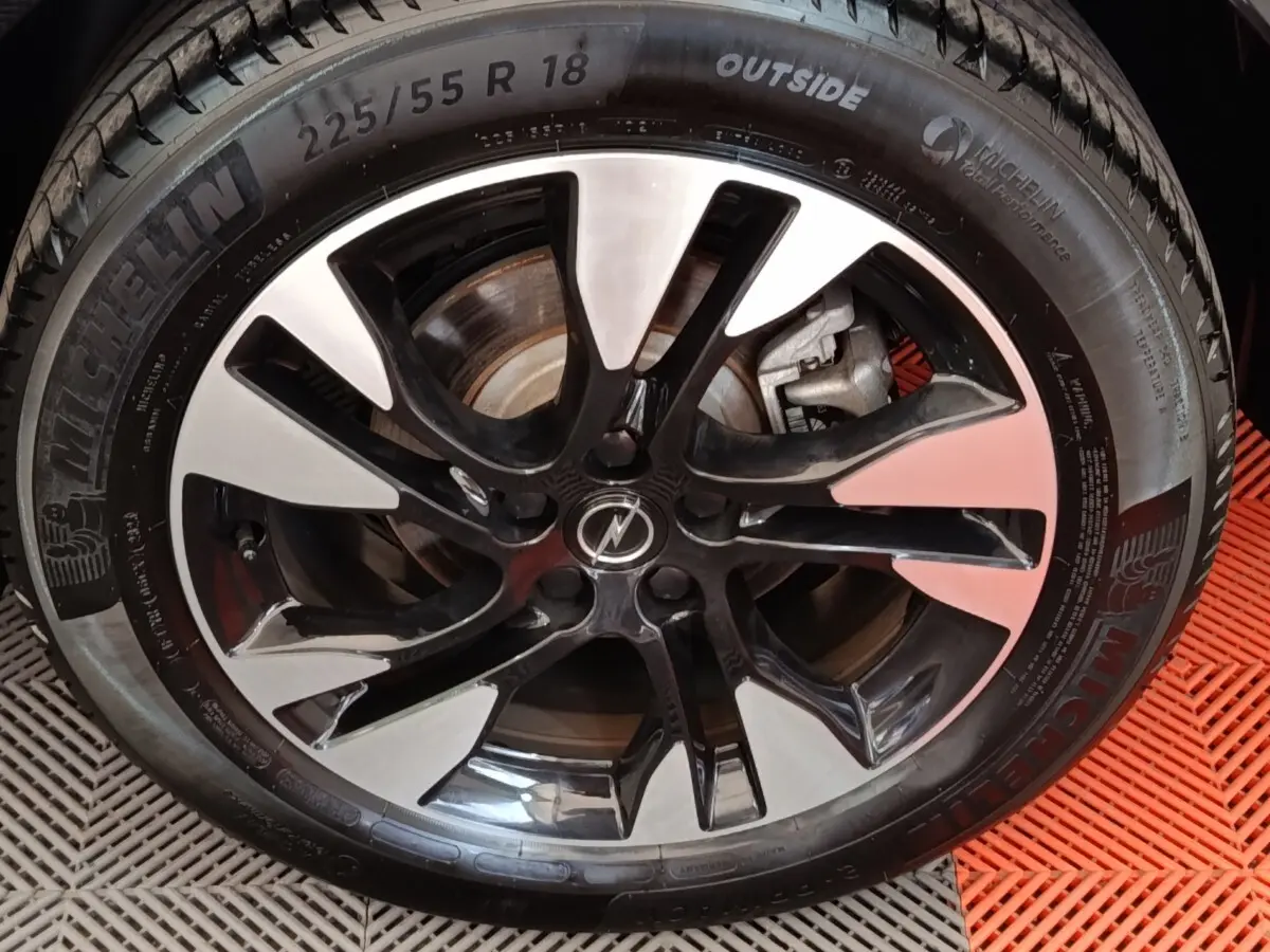 Gros plan sur la jante alu bicolore noire et argentée avec pneu Michelin du SUV Opel Grandland hybride 2023 noir.