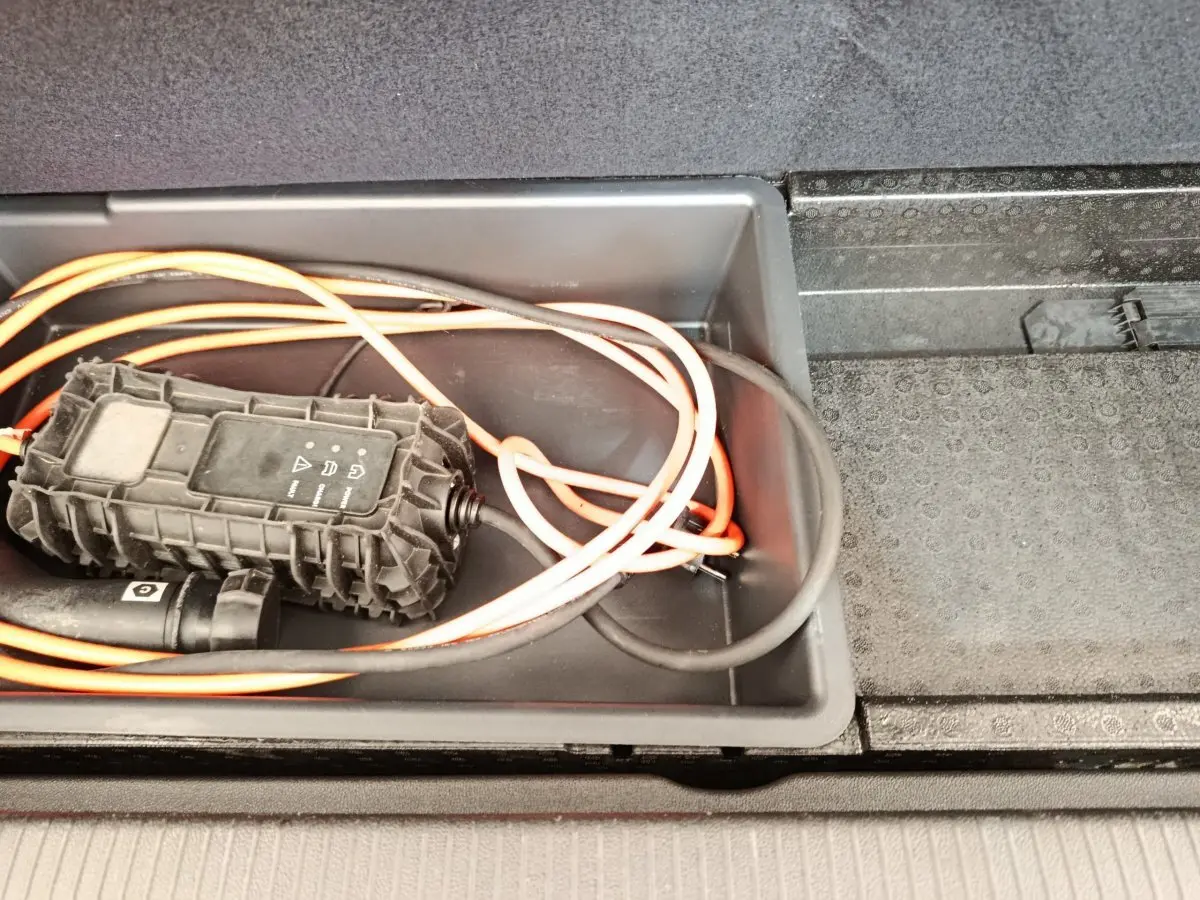 Gros plan sur le câble de charge orange et noir rangé dans le coffre du coffre d’un Opel Grandland hybride noir 2023.