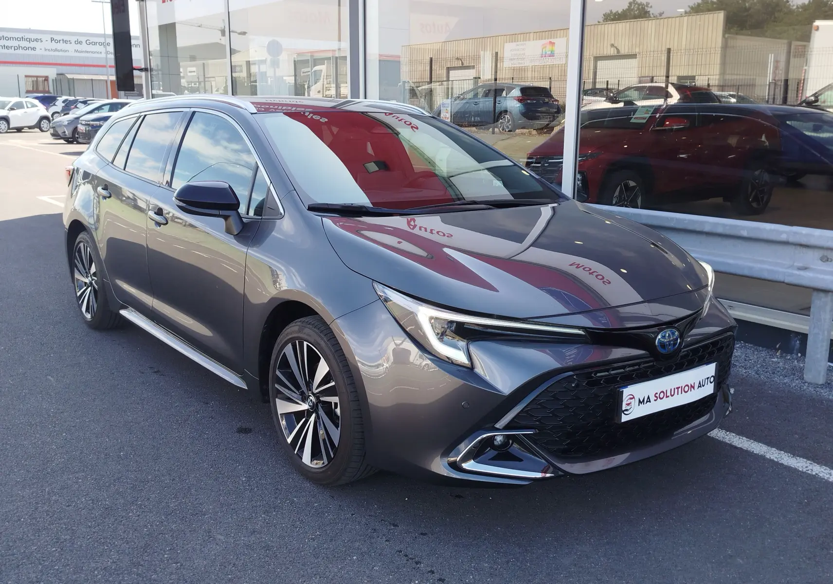 Toyota Corolla Touring Sport gris Atlas vue 3/4 avant droit, mettant en valeur sa calandre large et ses jantes alliage.