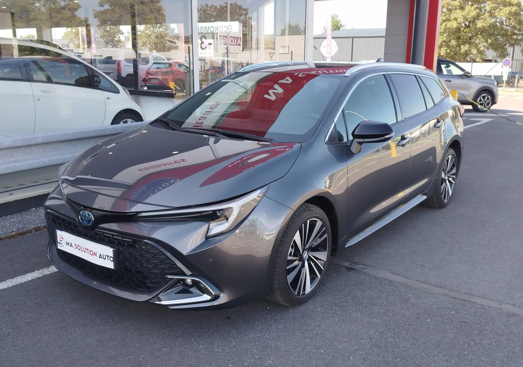 Toyota Corolla Touring Sport gris Atlas vue 3/4 avant droit, avec calandre noire et jantes alliage bicolores.