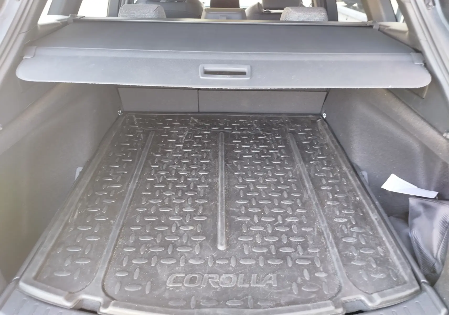 Vue intérieure du coffre de la Toyota Corolla Touring Sport 2026, tapis de protection noir marqué "COROLLA" visible.
