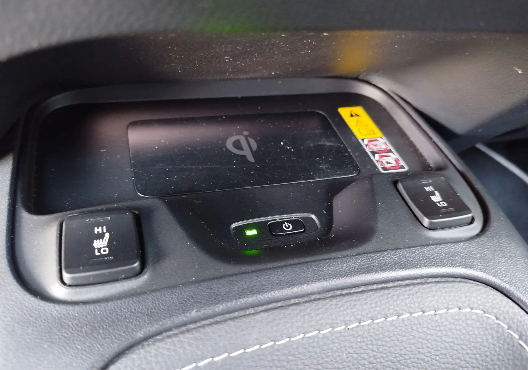 Gros plan sur la console centrale noire avec recharge sans fil et boutons de sièges chauffants de la Toyota Corolla Touring Sport.