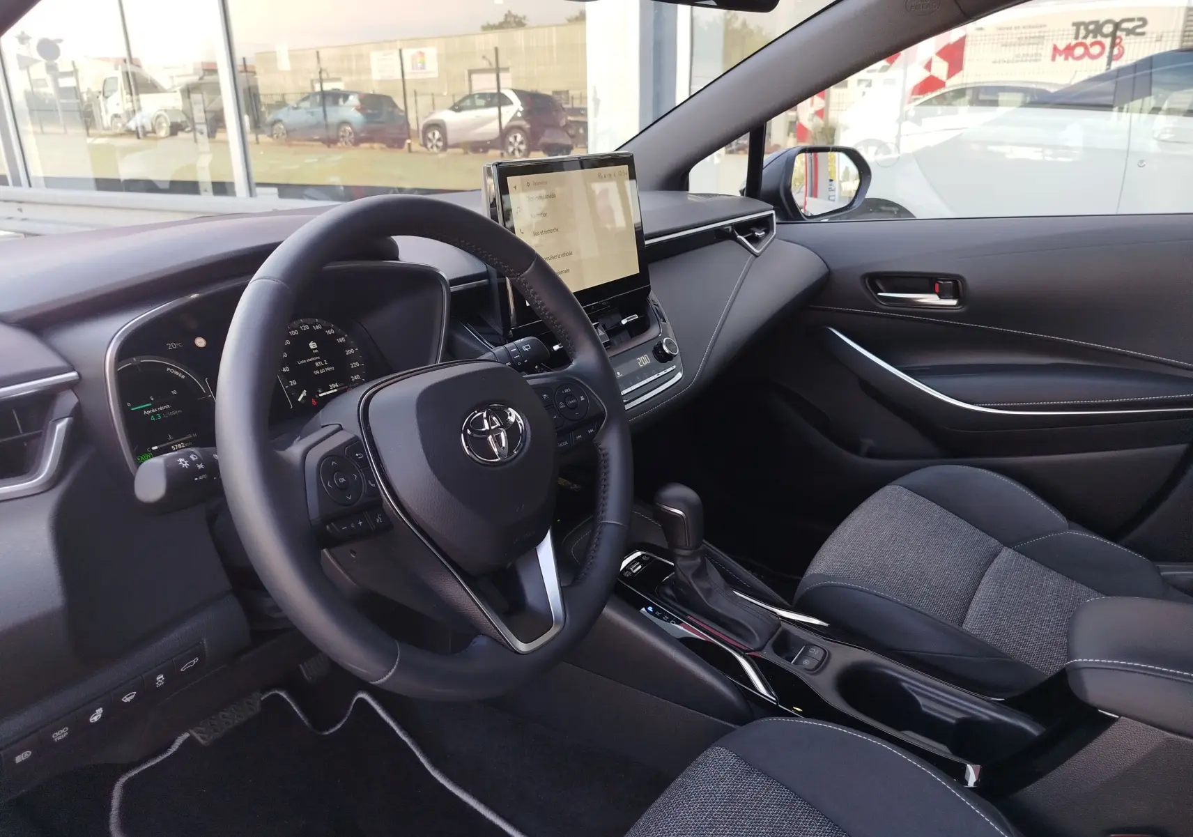 Intérieur de la Toyota Corolla Touring Sport 2026, vue côté conducteur, tableau de bord moderne avec écran tactile central.