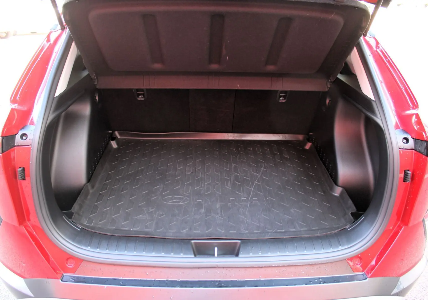 Coffre ouvert vu de l'arrière d'un Hyundai Kona 2024 rouge Ultimate Metal avec tapis de coffre noir.
