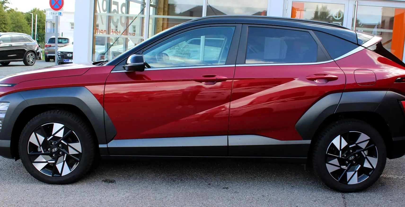 Vue latérale gauche du Hyundai Kona 2024 rouge Ultimate Metal avec toit noir et jantes bicolores distinctives.