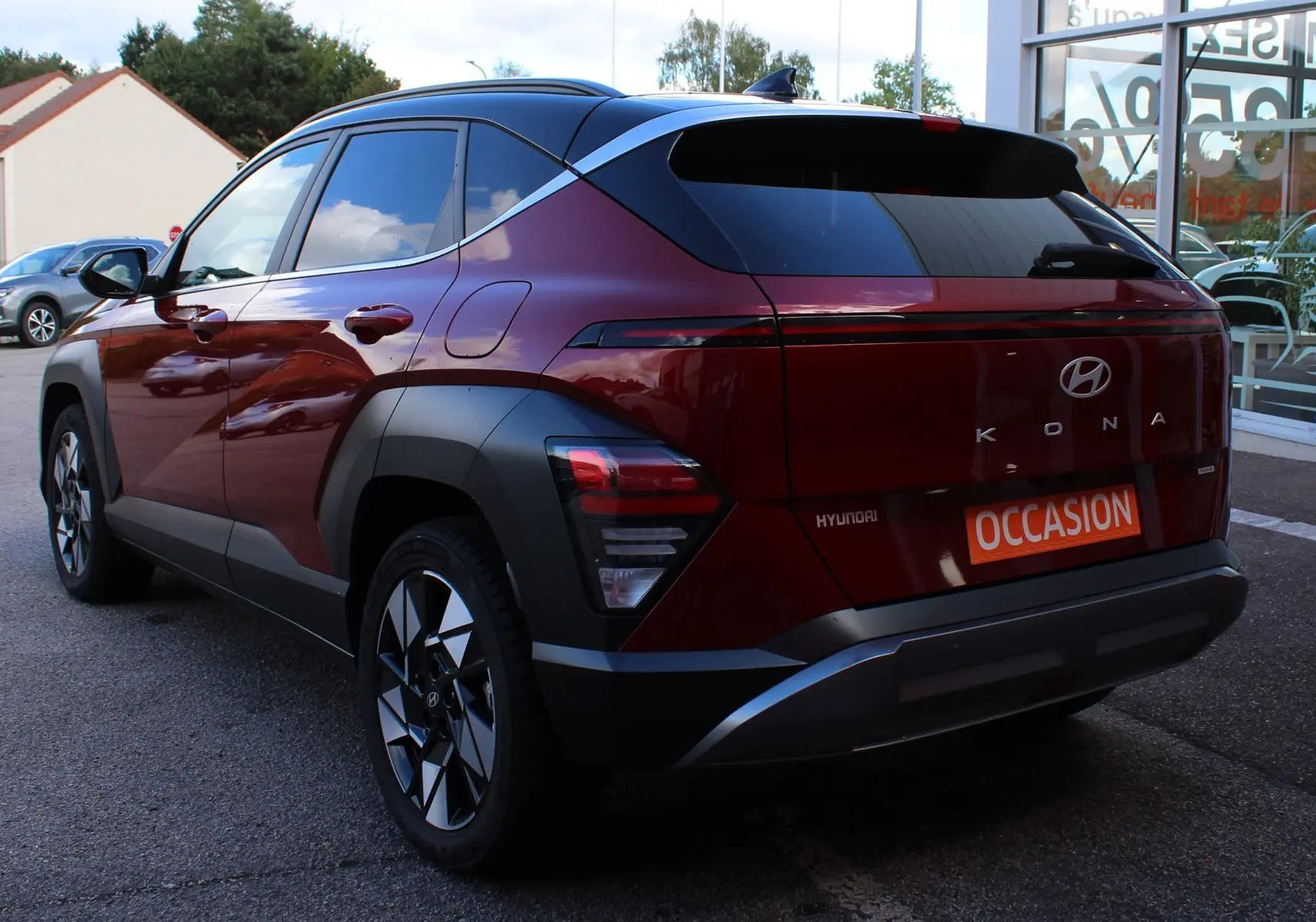 Vue 3/4 arrière gauche d'un Hyundai Kona 2024 rouge Ultimate Metal avec toit noir et jantes bicolores.