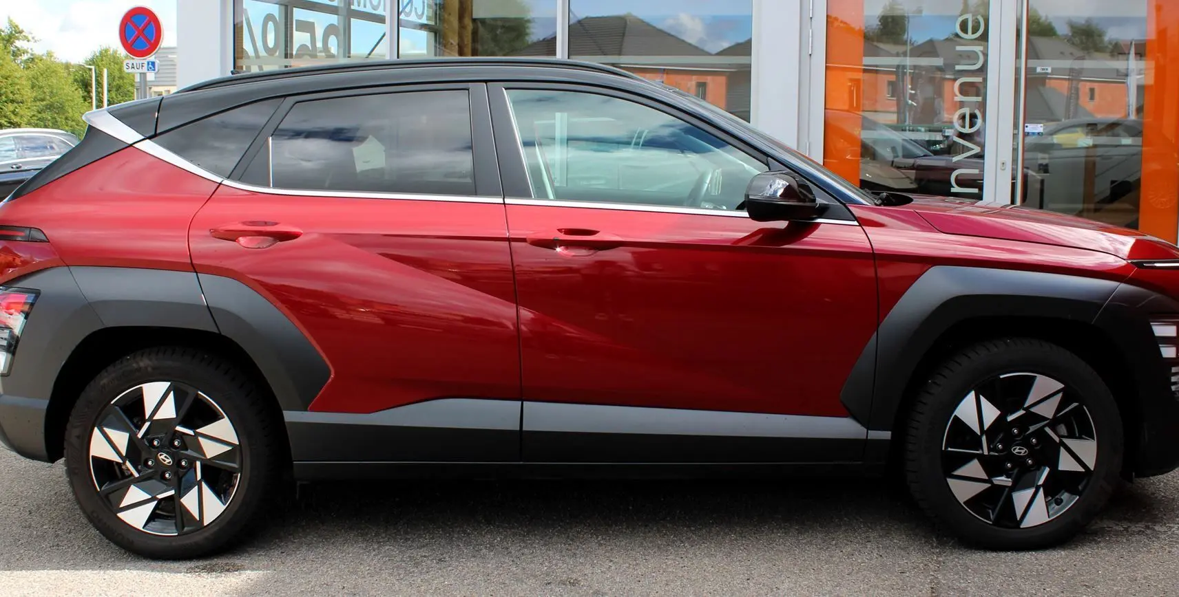 Vue de profil côté gauche du Hyundai Kona 2024 rouge Ultimate Metal avec toit noir et jantes bicolores distinctives.