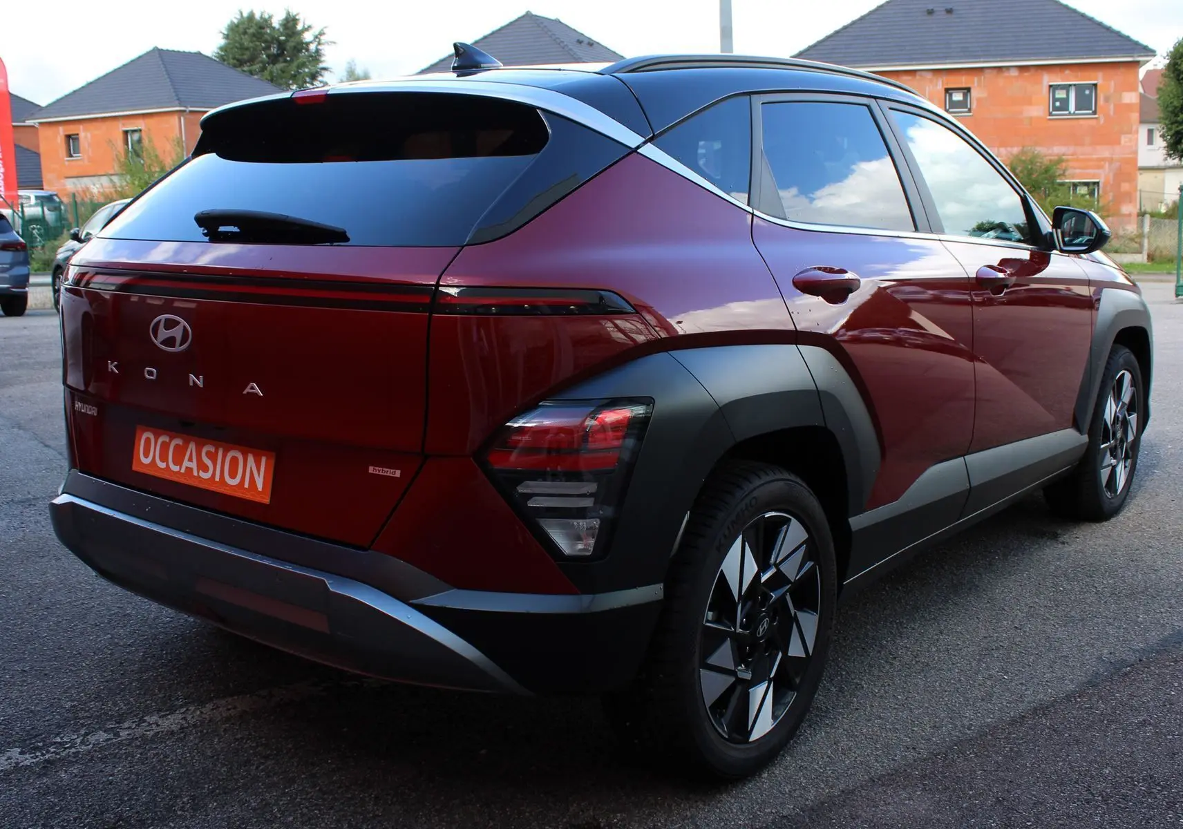Vue 3/4 arrière droite d'un Hyundai Kona 2024 rouge Ultimate Metal avec toit noir et jantes bicolores.