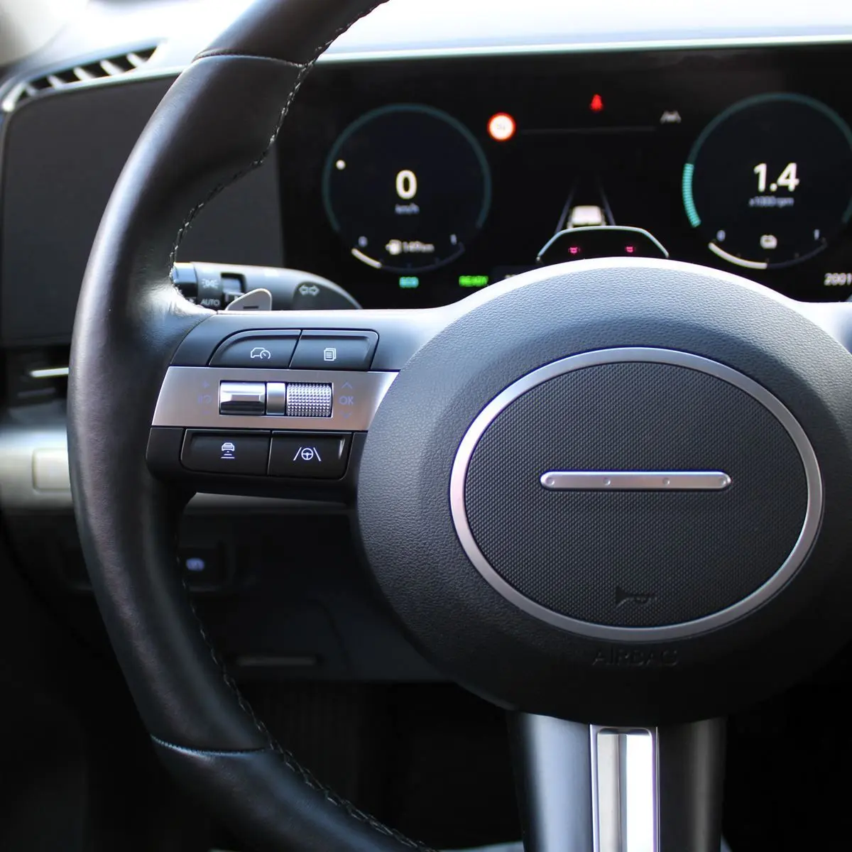 Gros plan sur le volant noir et les commandes multifonctions du Hyundai Kona 2024 avec tableau de bord numérique en arrière-plan.