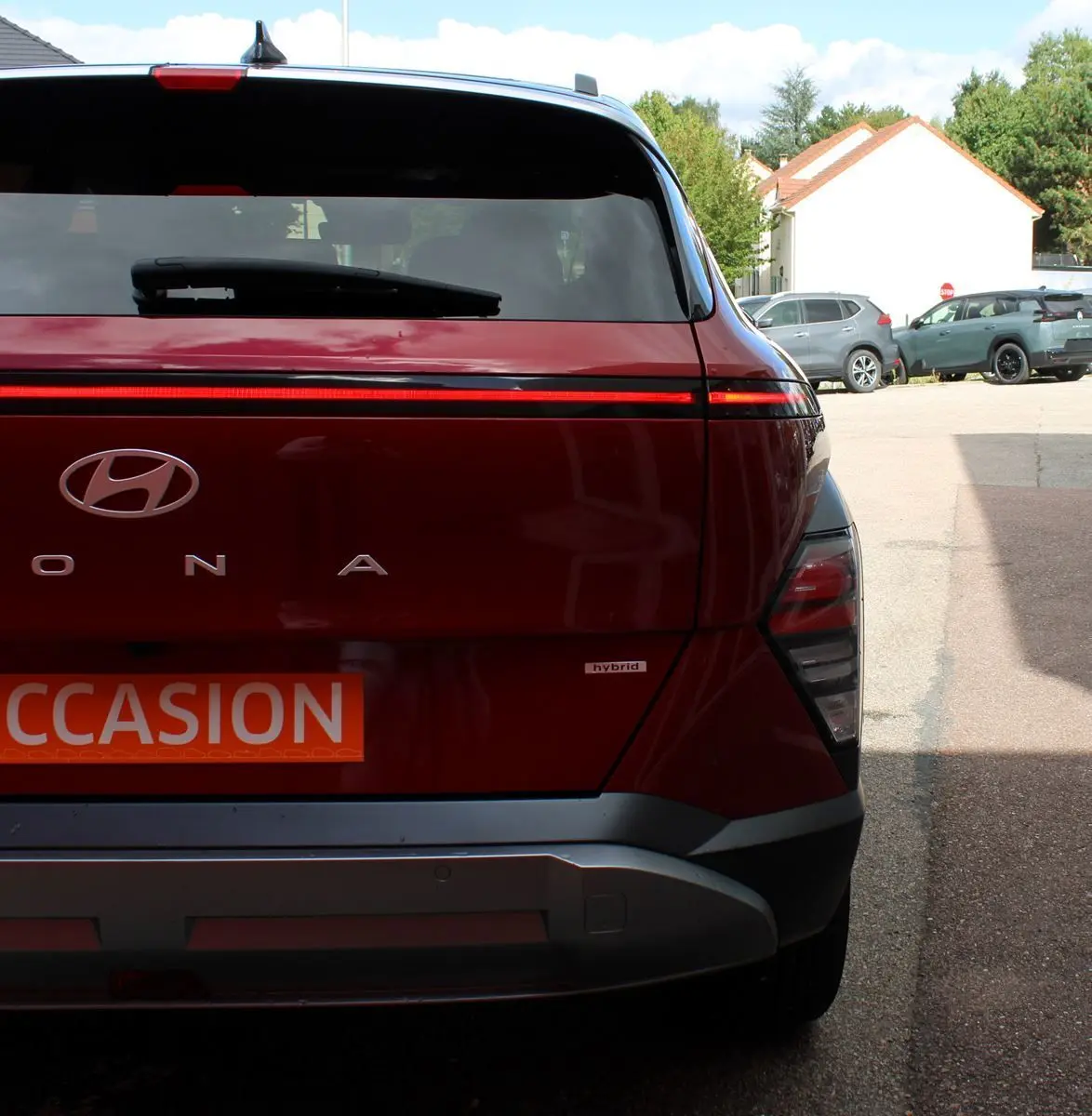 Vue arrière d'un Hyundai Kona rouge Ultimate Metal avec bande lumineuse LED et logo hybride visible sur un parking.