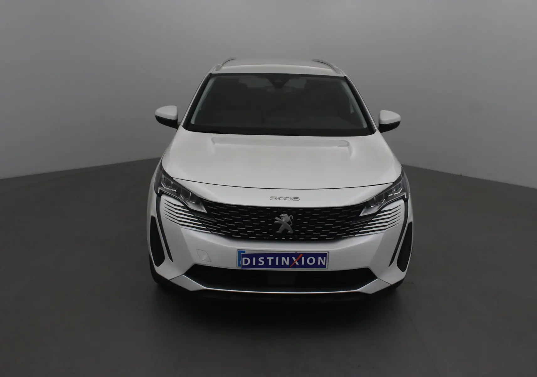 Vue frontale d'un Peugeot 5008 blanc nacré avec calandre noire et logo lion distinctif sur fond neutre.