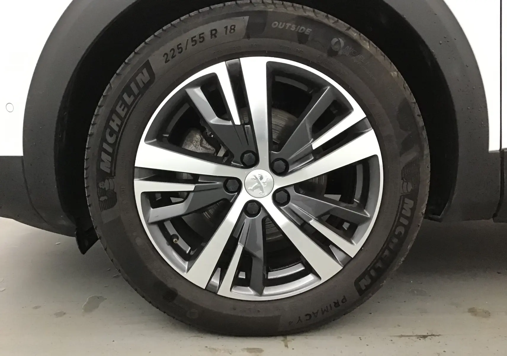 Gros plan sur la roue avant gauche du Peugeot 5008 blanc nacré, jante alliage 18 pouces au design moderne.