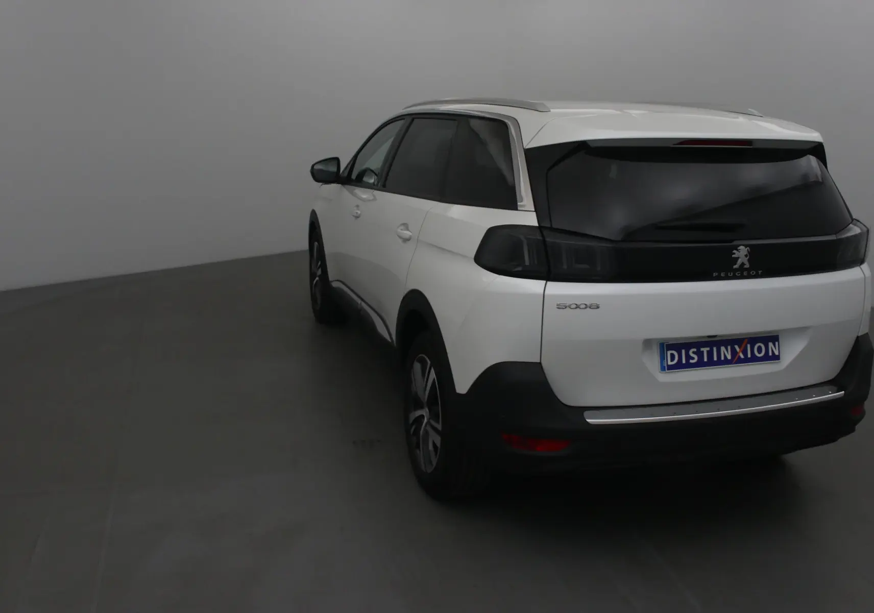 Vue 3/4 arrière gauche d'un Peugeot 5008 blanc nacré avec vitres teintées et feux arrière noirs dans un studio.