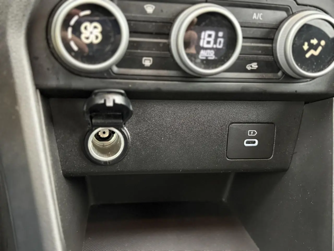 Gros plan sur la console centrale du Dacia Jogger 2025, montrant la prise allume-cigare et un port USB-C de recharge.
