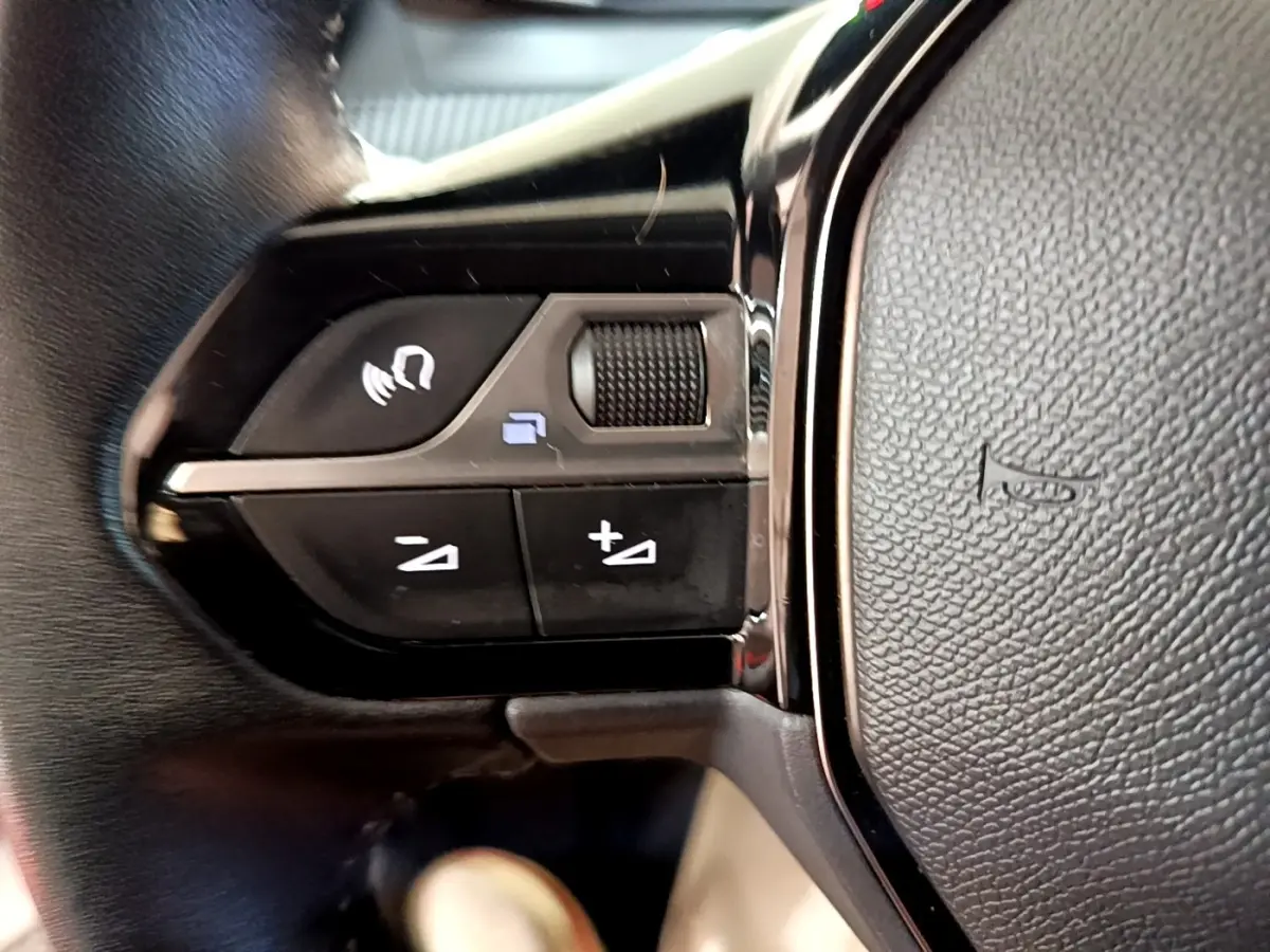Gros plan sur les commandes vocales et volume au volant cuir noir de la Peugeot 208 électrique blanche.