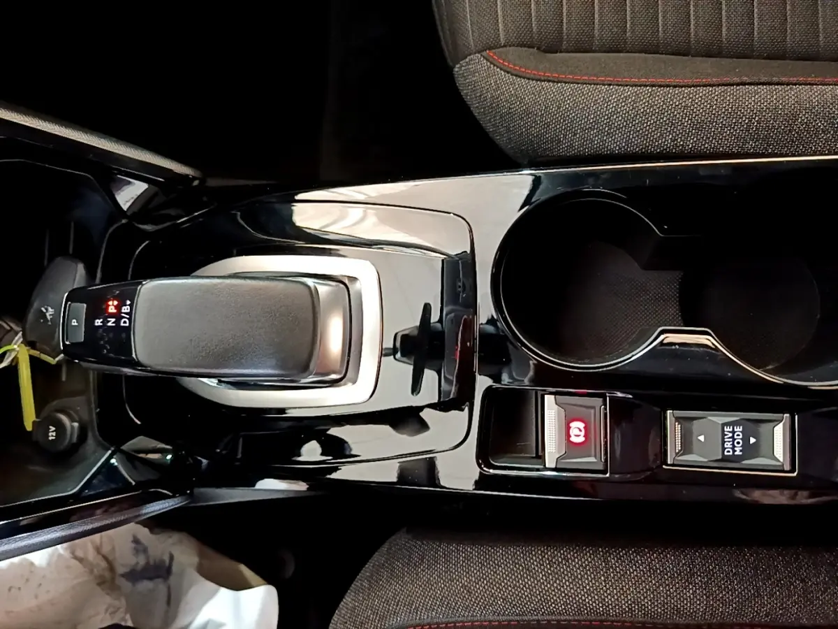 Vue rapprochée de la console centrale noire brillante avec levier de vitesse automatique et boutons Drive Mode et frein à main électrique d'une Peugeot 208 blanche.