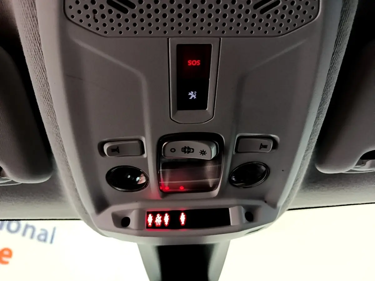Vue en gros plan du plafonnier intérieur gris avec bouton SOS rouge et commandes d’éclairage de la Peugeot 208 Electrique blanche.