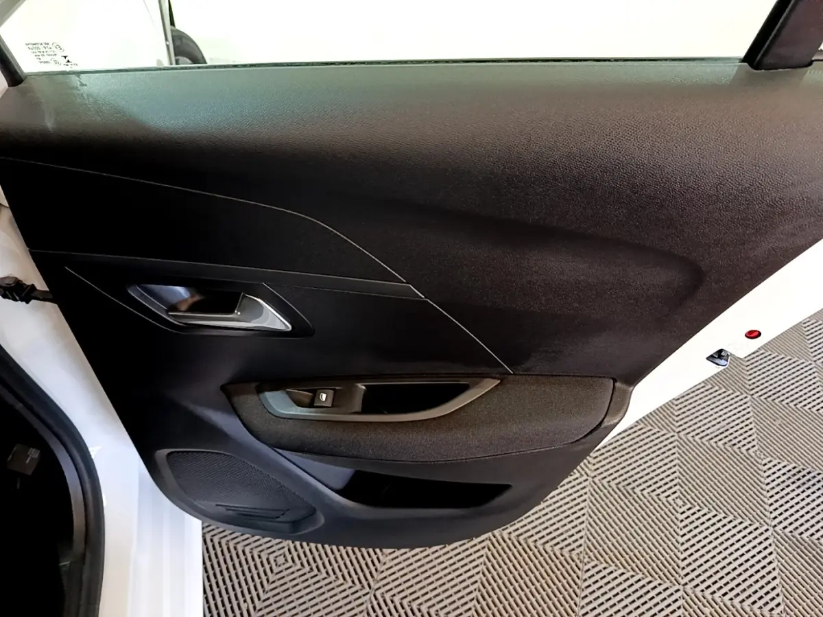 Vue rapprochée de la porte arrière droite noire avec poignée intérieure argentée d’une Peugeot 208 électrique blanche.