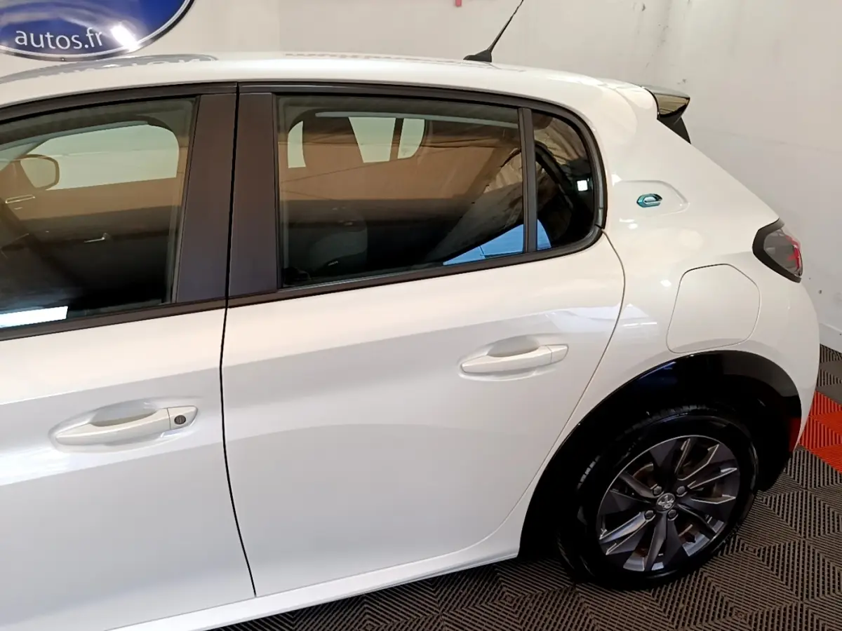 Vue latérale droite d'une Peugeot 208 électrique blanche, avec badge "e" distinctif sur l'aile arrière.