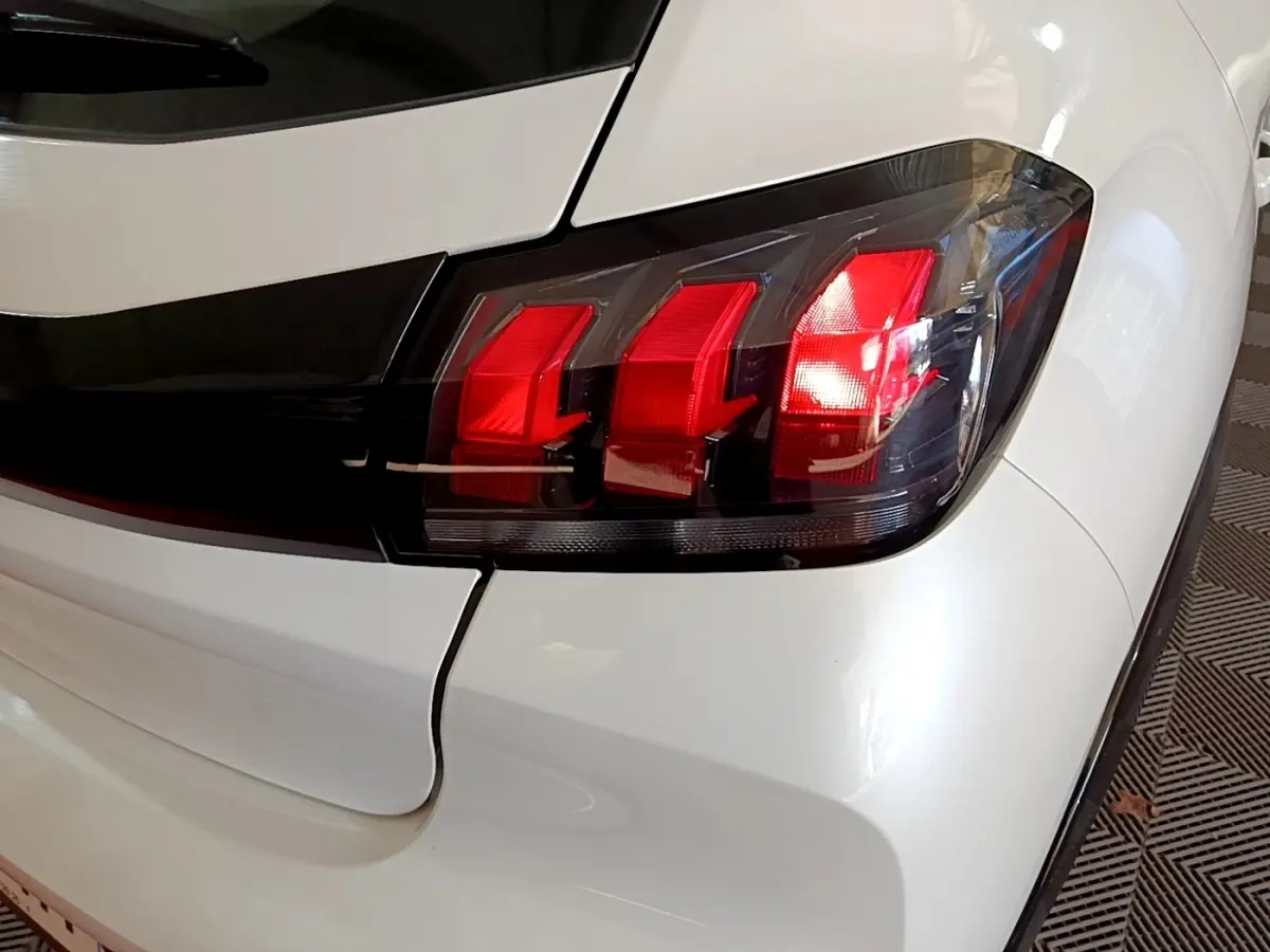 Gros plan sur le feu arrière droit rouge et noir d'une Peugeot 208 électrique blanche, version Active Business.