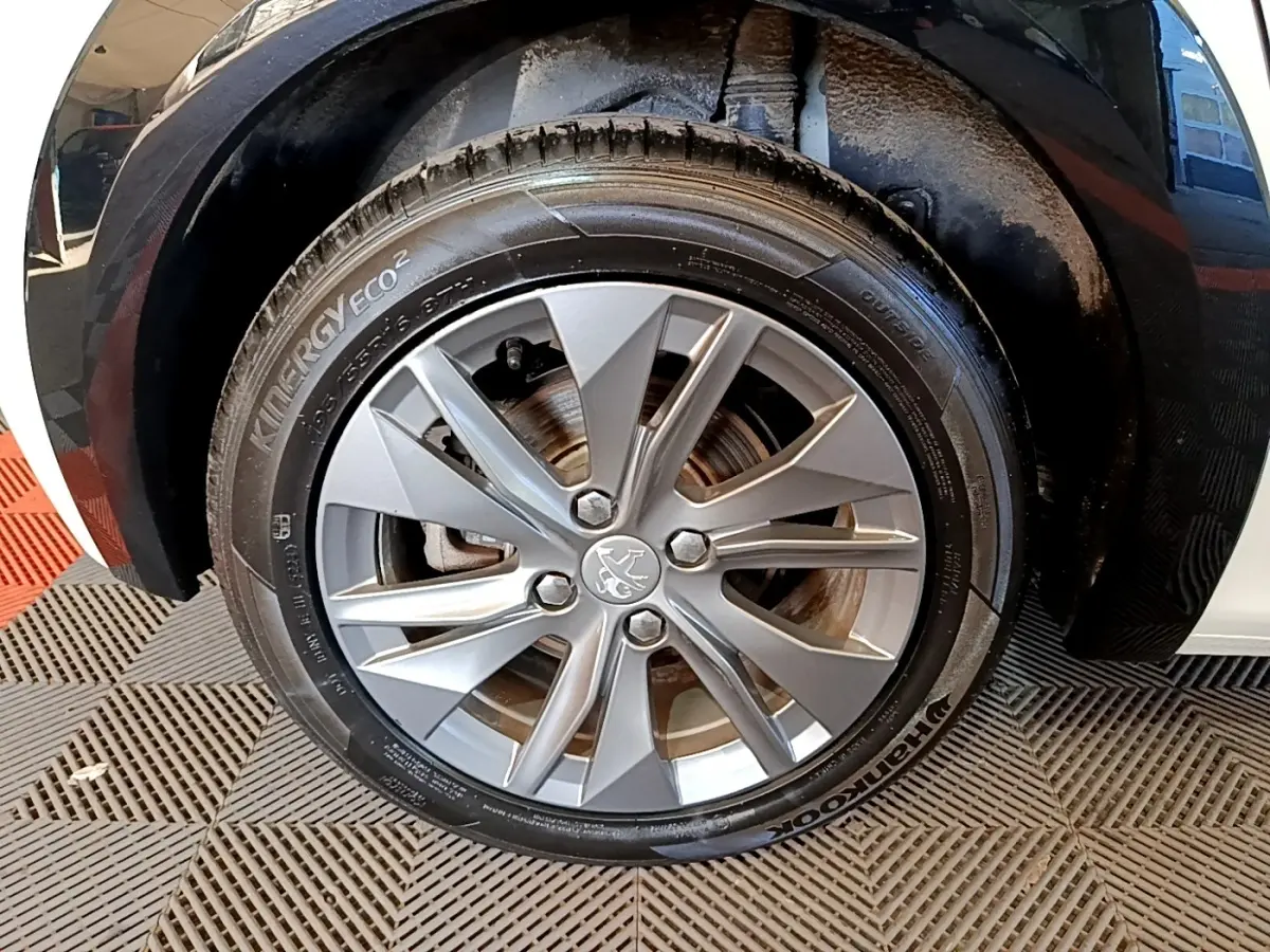 Gros plan sur la roue avant gauche de la Peugeot 208 électrique blanche, mettant en valeur la jante alu et le logo lion central.