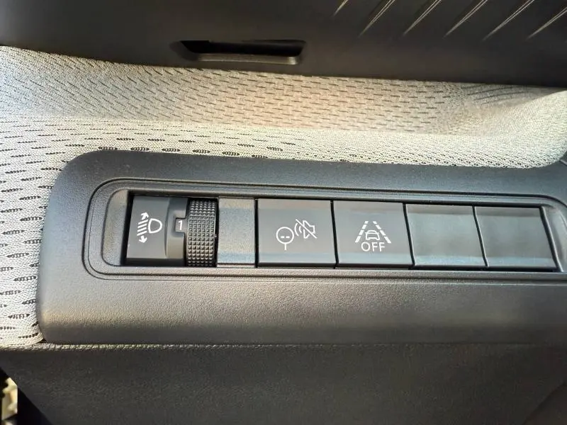 Gros plan sur les commandes noires de réglage des phares et aides à la conduite dans l’habitacle d’une Citroën C3 Electrique noir Perla Nera.