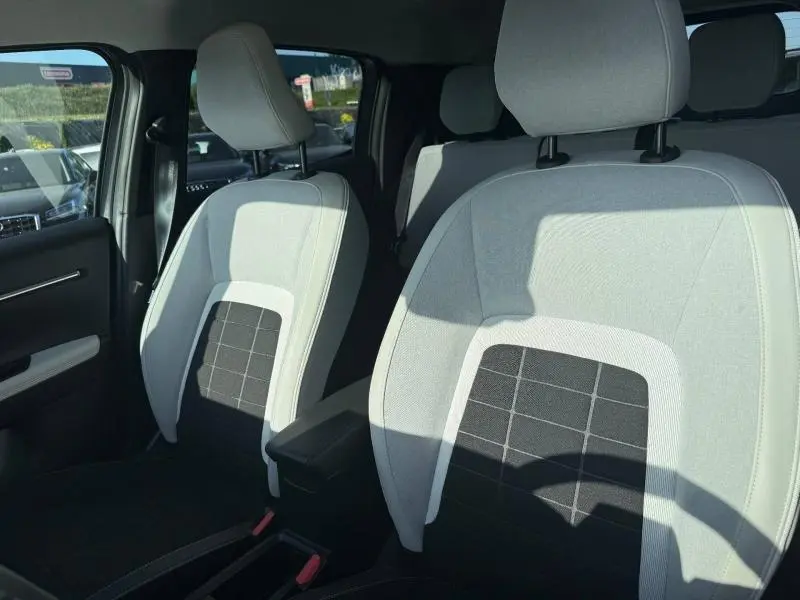 Vue intérieure sur les sièges avant gris clair et noir de la Citroën C3 électrique 2025 avec accoudoir central.